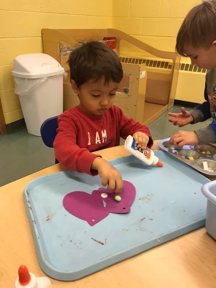 Child gluing decorations onto a purple heart shape