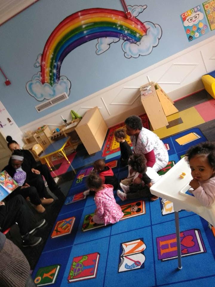 Adults and children sitting on a colorful rug in a classroom