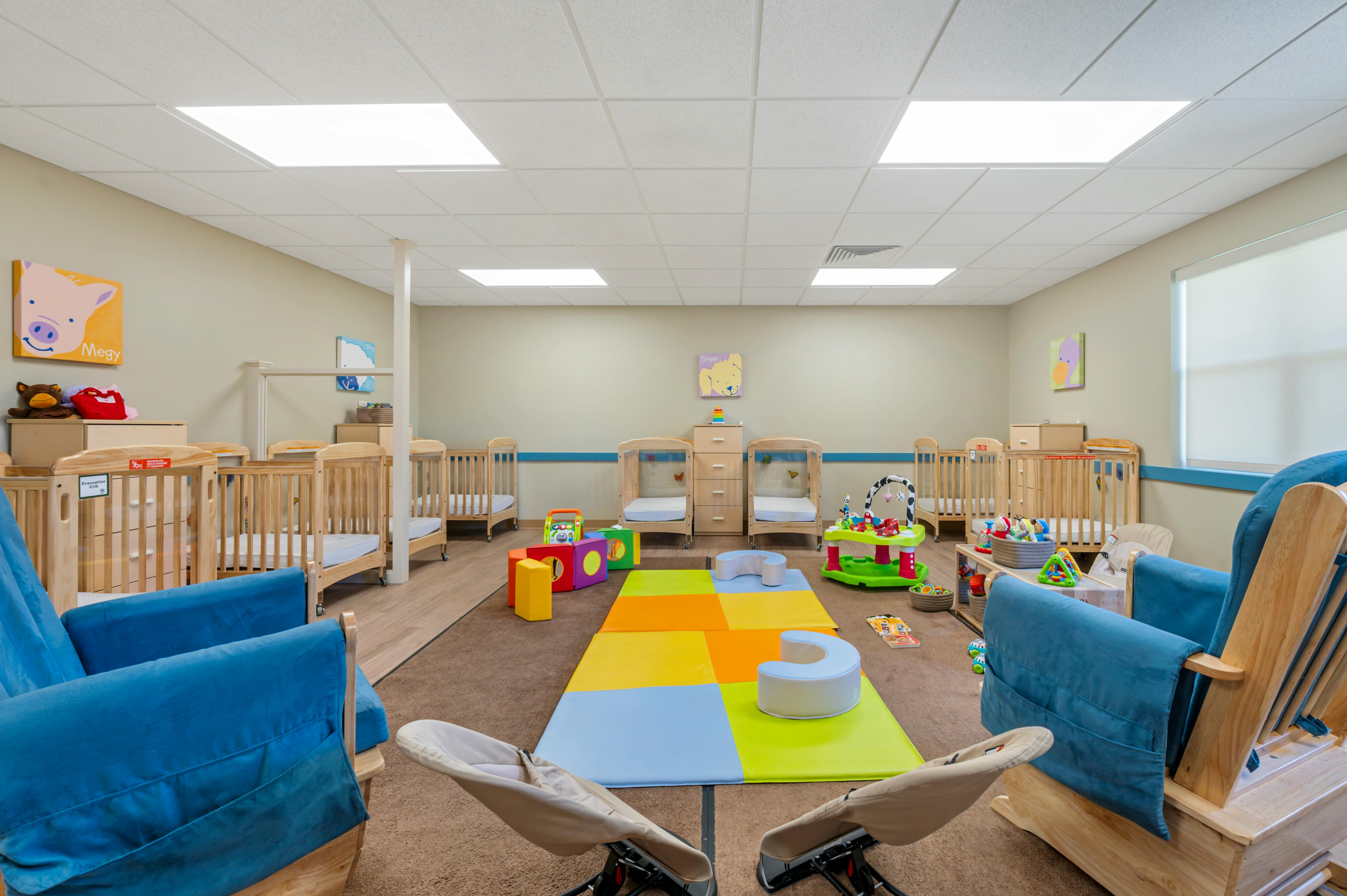 A childcare room with several cribs, playmats, and toys