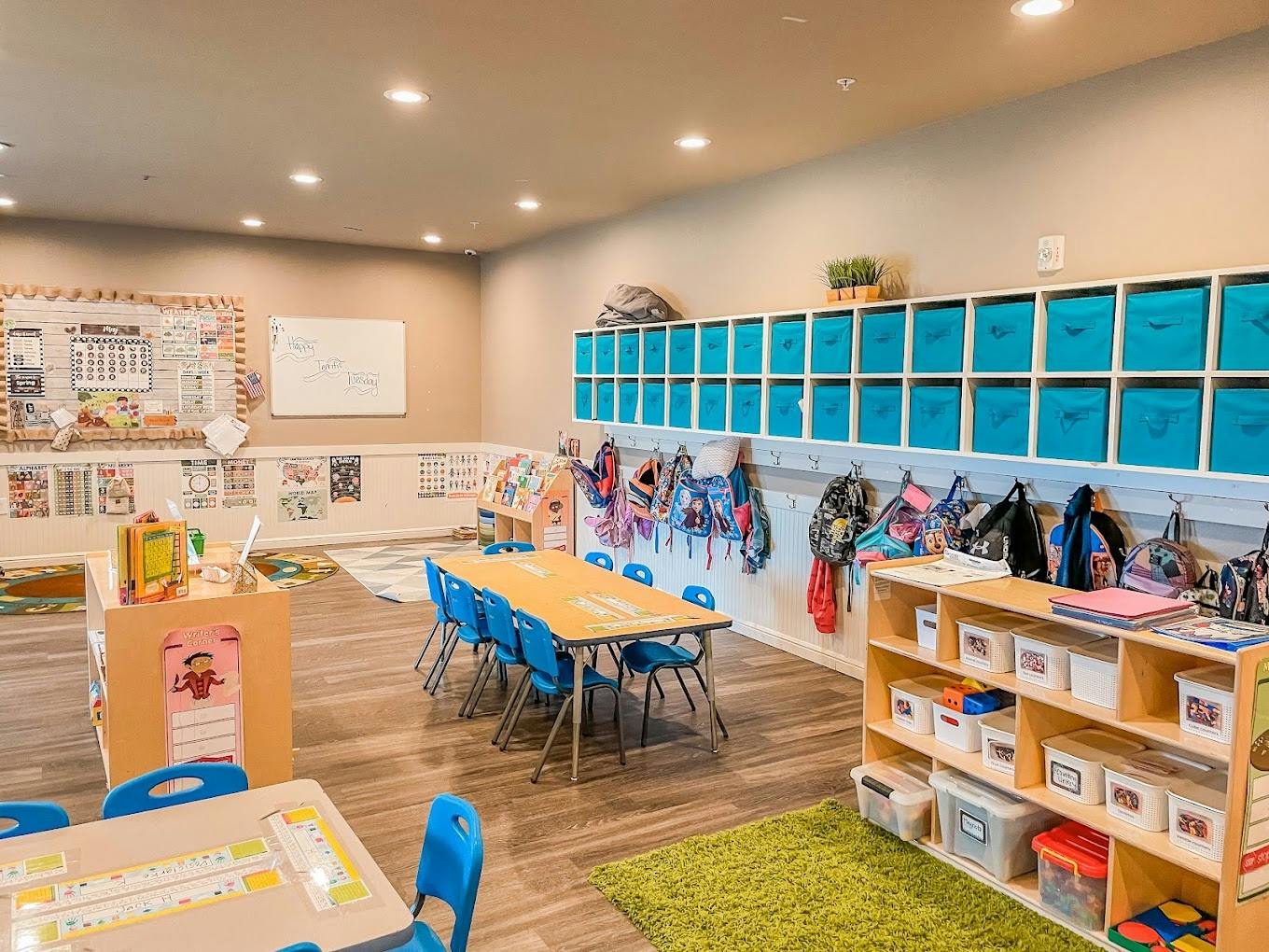 Classroom interior with tables, chairs, storage bins, and backpacks