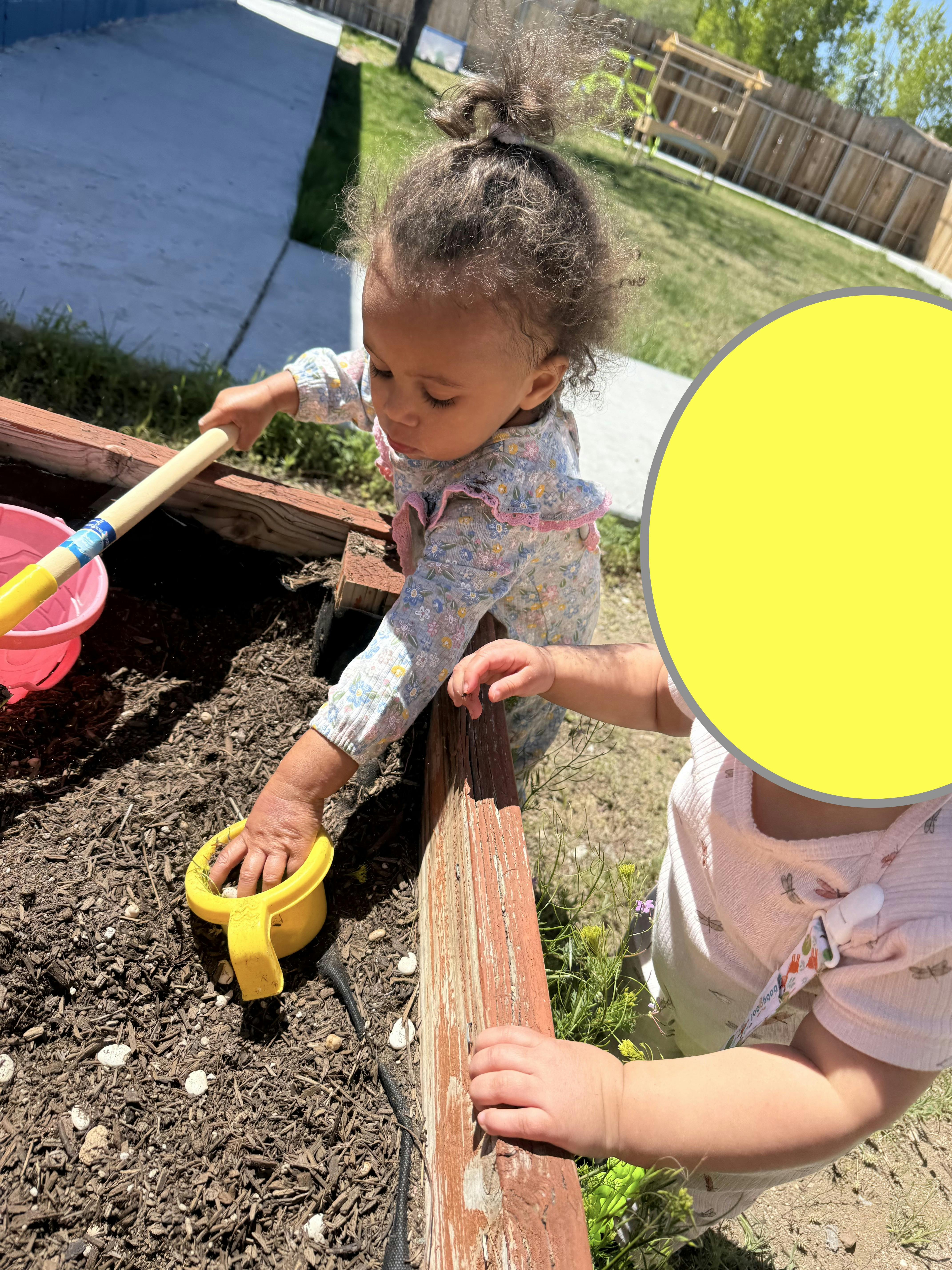 Child playing in dirt with a yellow toy watering can and a shovel
