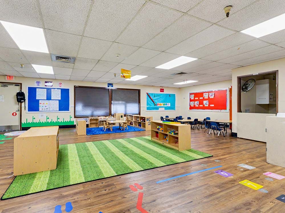 Empty classroom with small tables and chairs, and a green striped rug