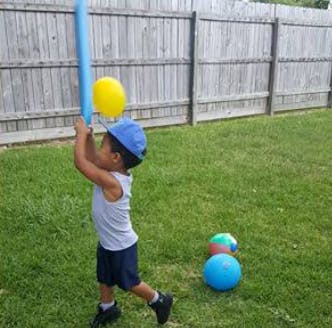 Child holding a blue bat and yellow balloon in a grassy yard