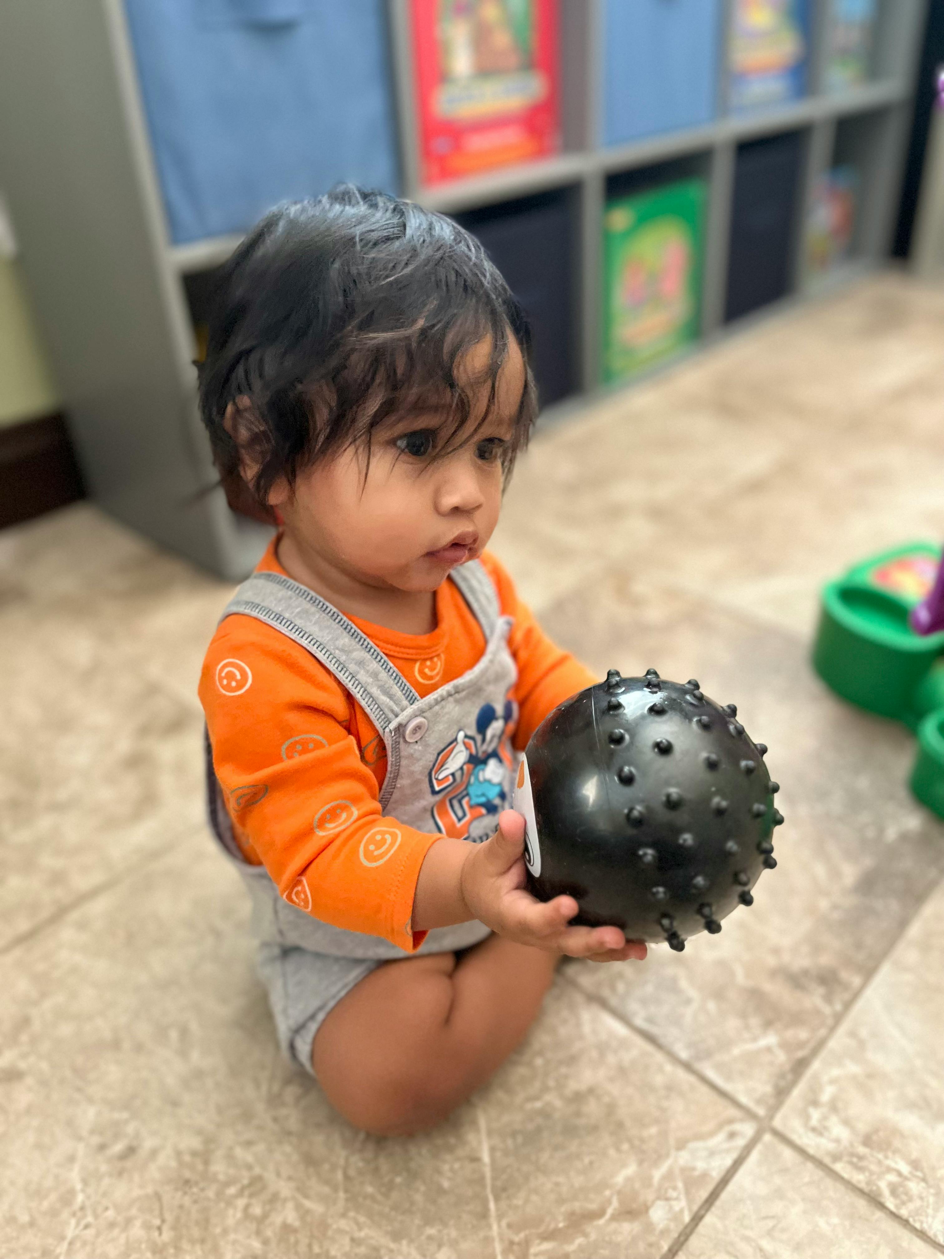 Child sitting on floor holding a black spiky ball