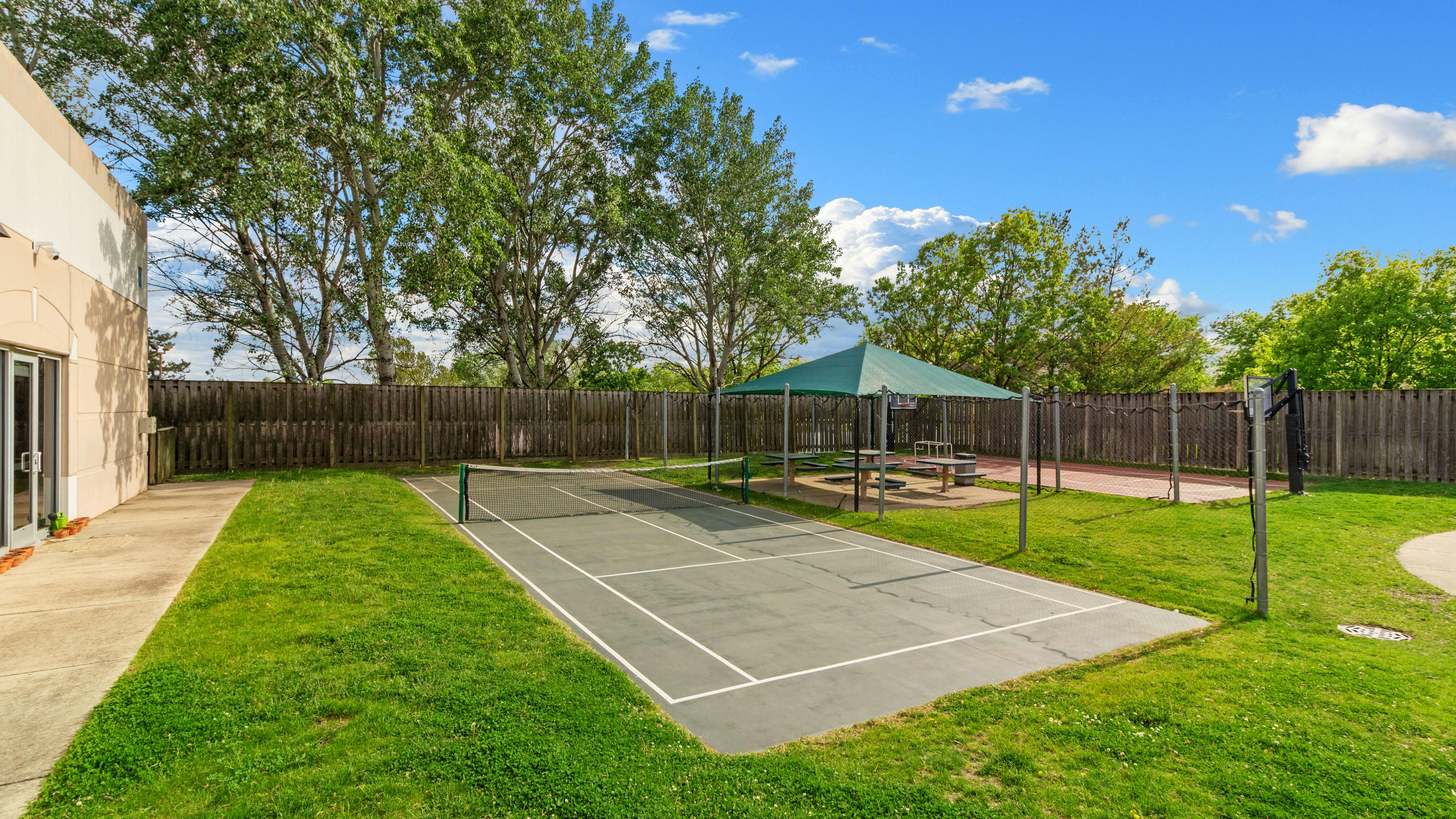 Outdoor area with a tennis court, a picnic area with a green canopy, and a basketball hoop