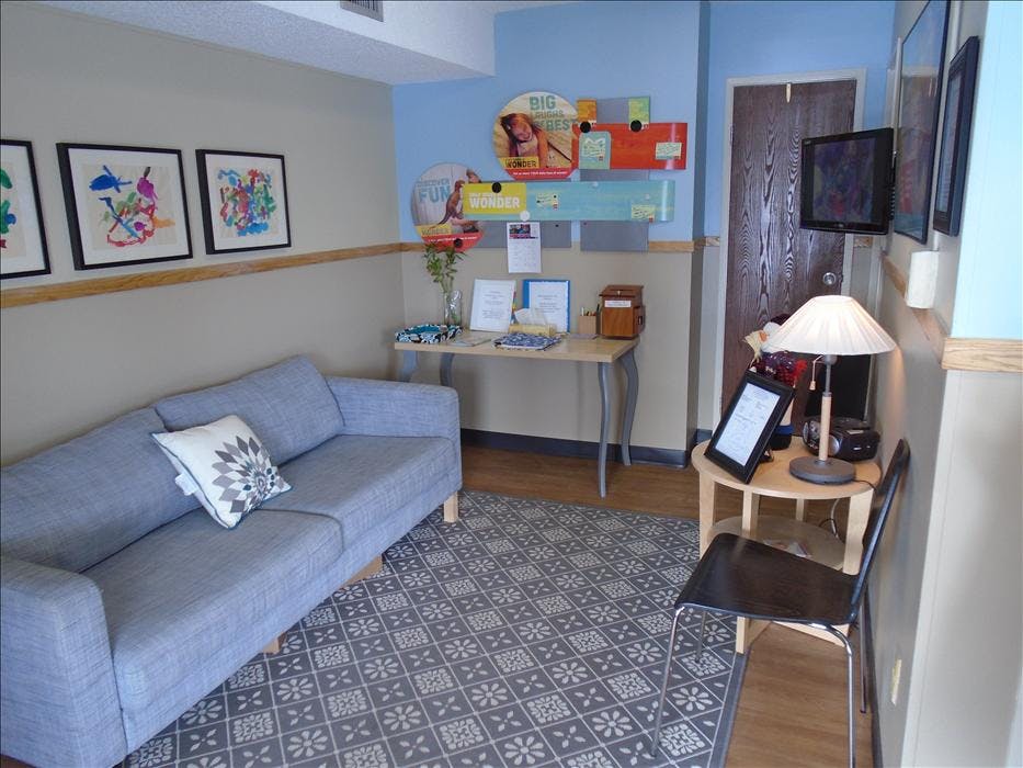 A waiting room with a sofa, end tables, lamps, and wall decor
