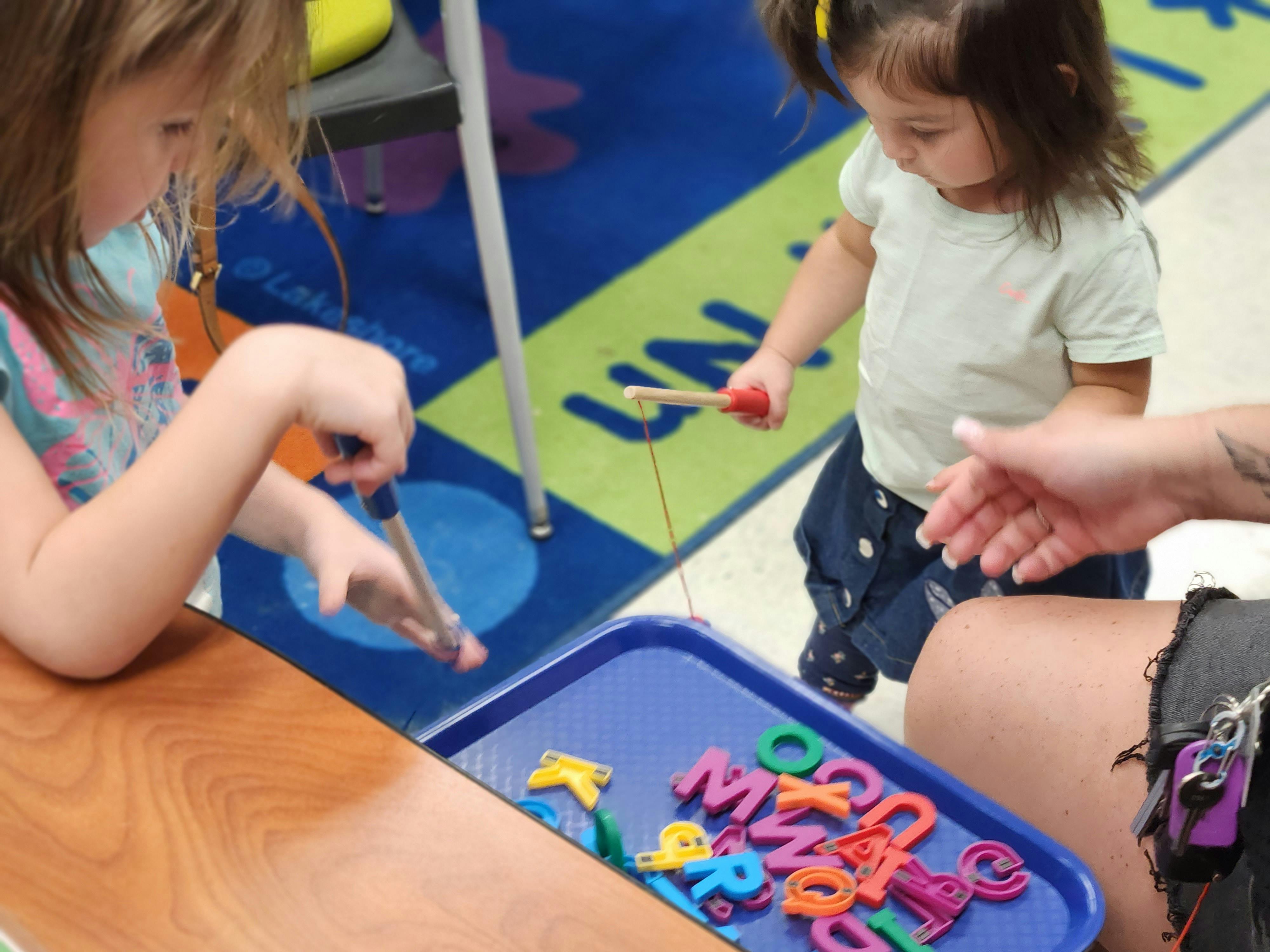 Two children playing with colorful letter magnets on a blue tray