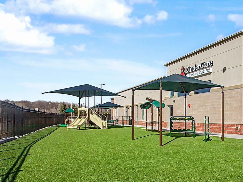 KinderCare building with a playground on artificial turf with shade structures and shade structures