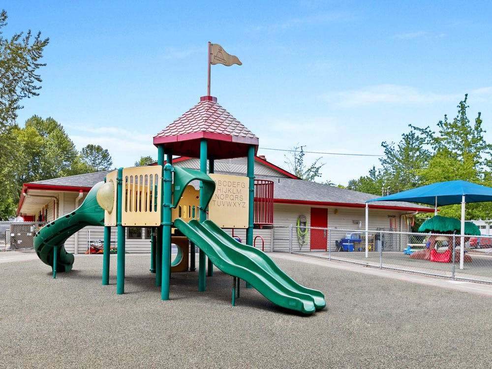 A playground with a large climbing structure and slides, with a building in the background