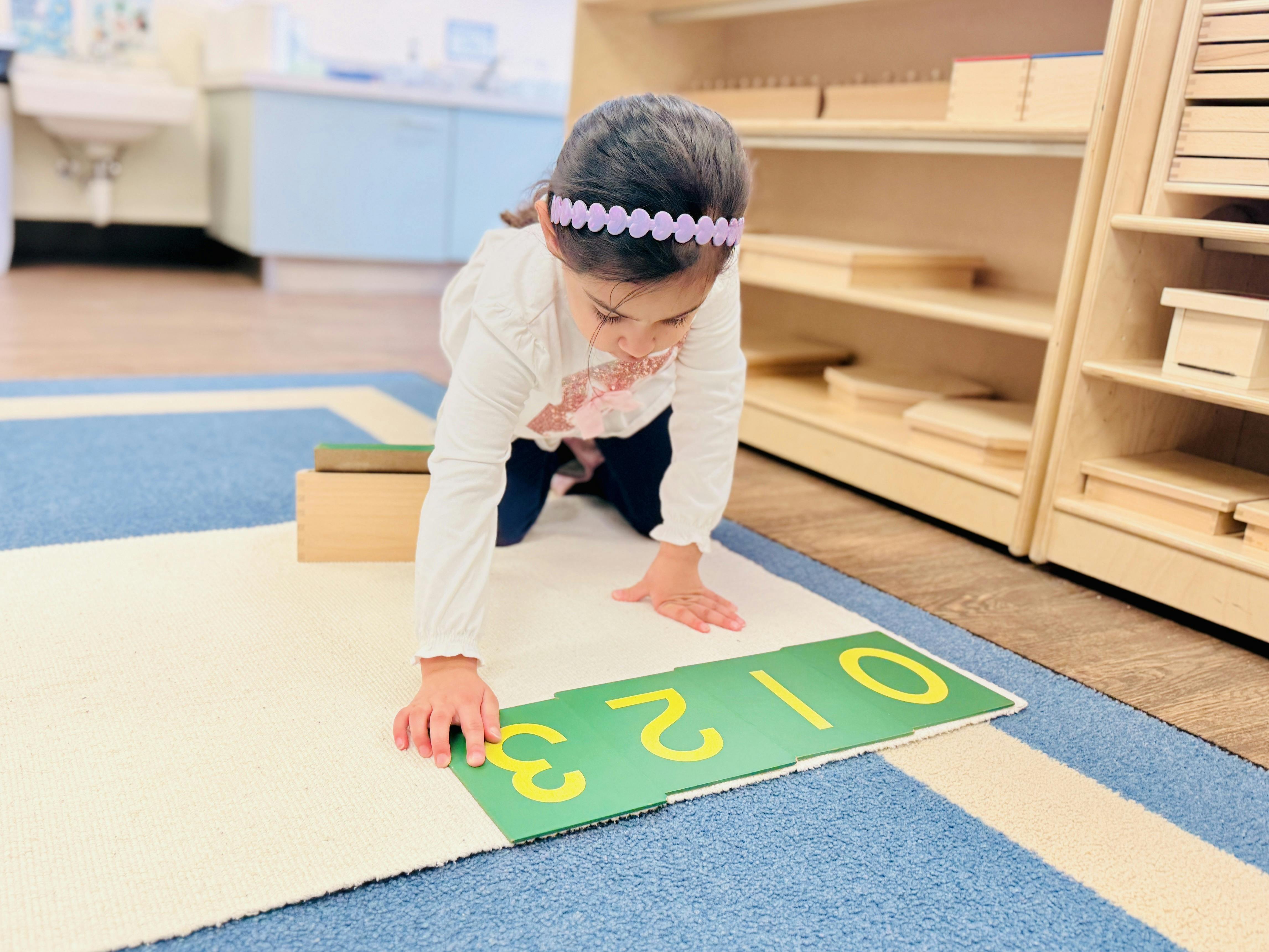 Child on hands and knees touching a green card with the number 3 on it