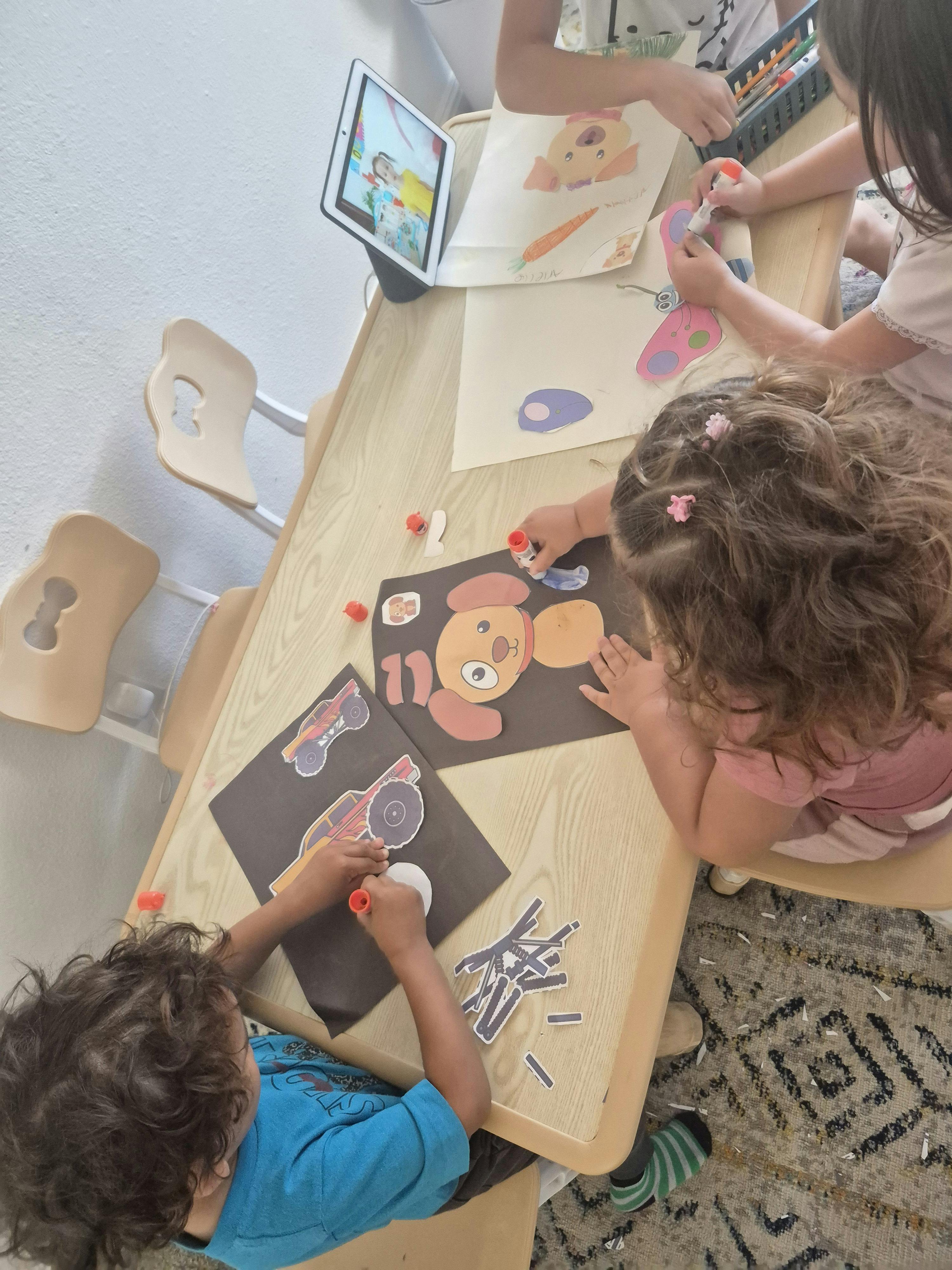 Children doing crafts at a table with glue sticks and paper cutouts