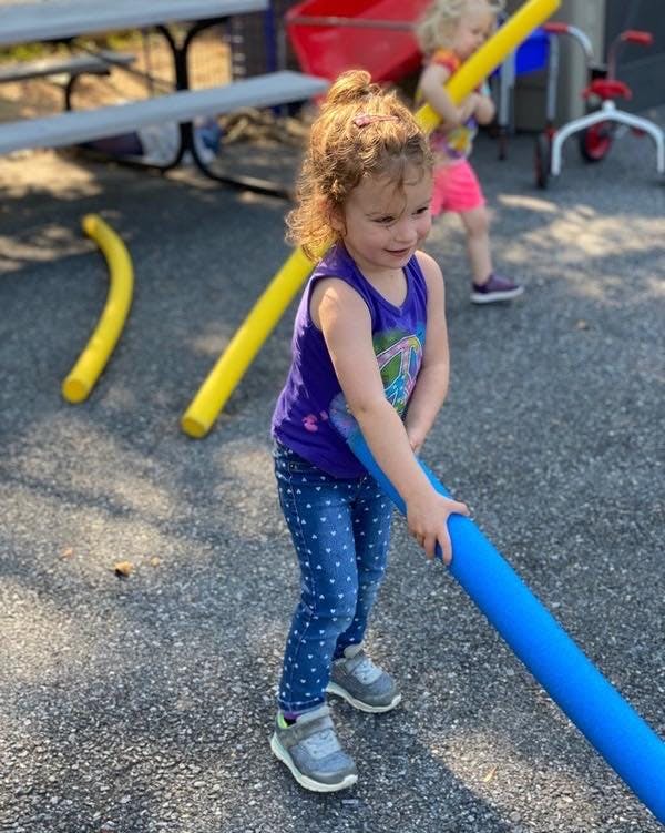 Child holding a blue pool noodle outdoors