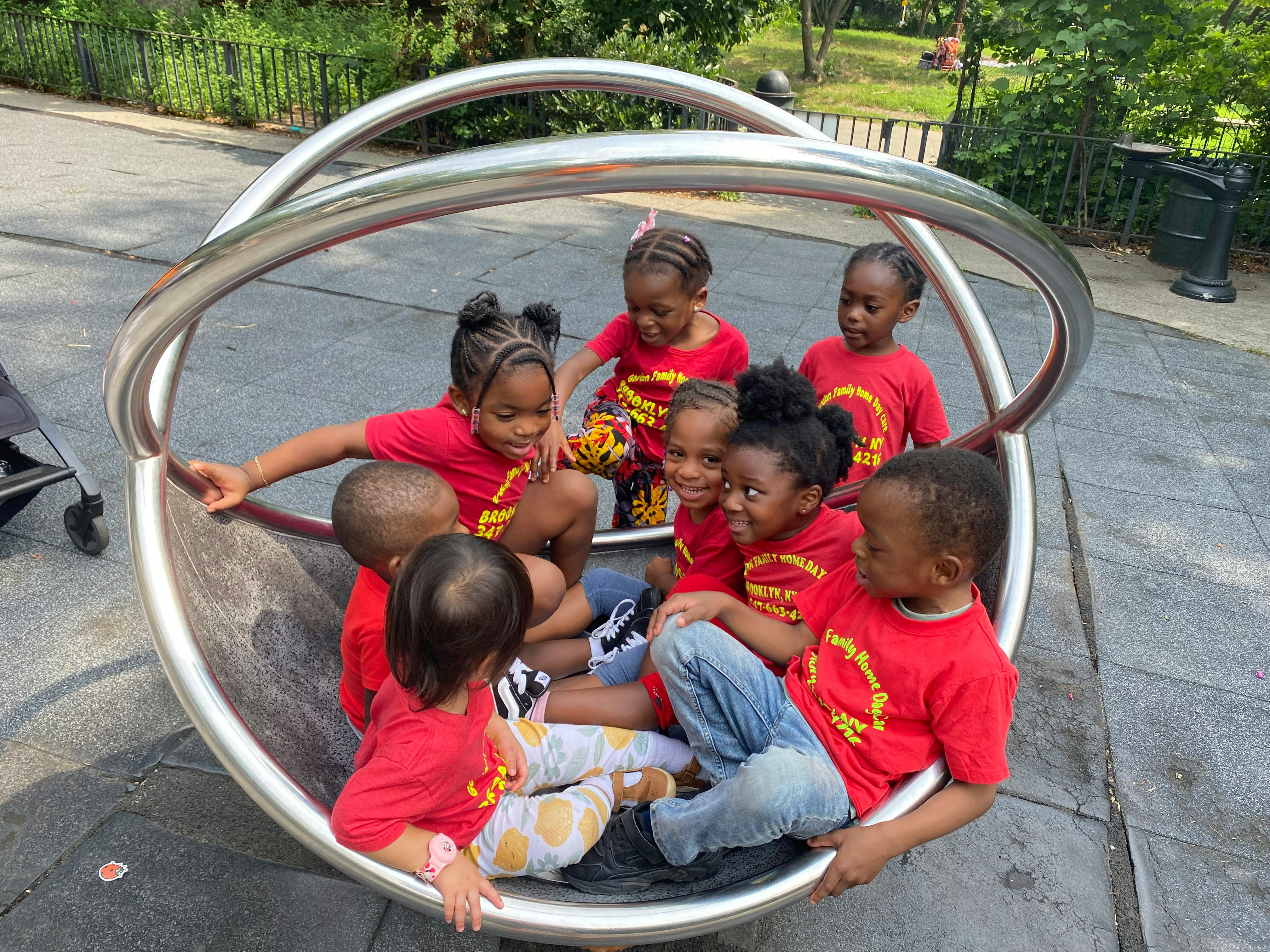 Group of children in red shirts sitting inside a circular metal playground toy