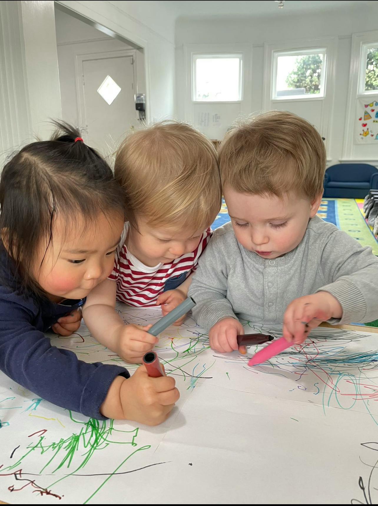 Three children drawing on paper with markers