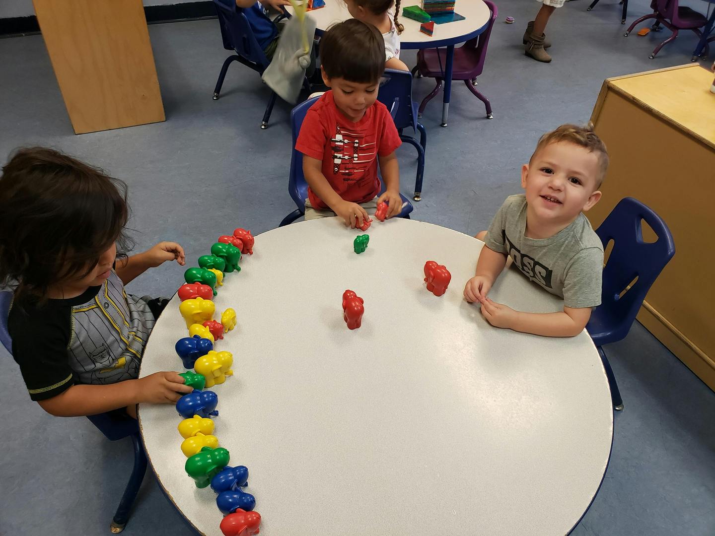 Three children playing with colorful plastic toys at a round table