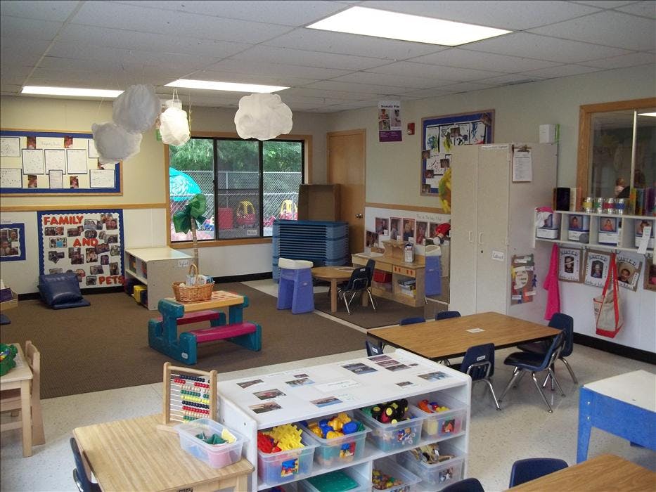 empty preschool classroom with small tables, chairs, and play items