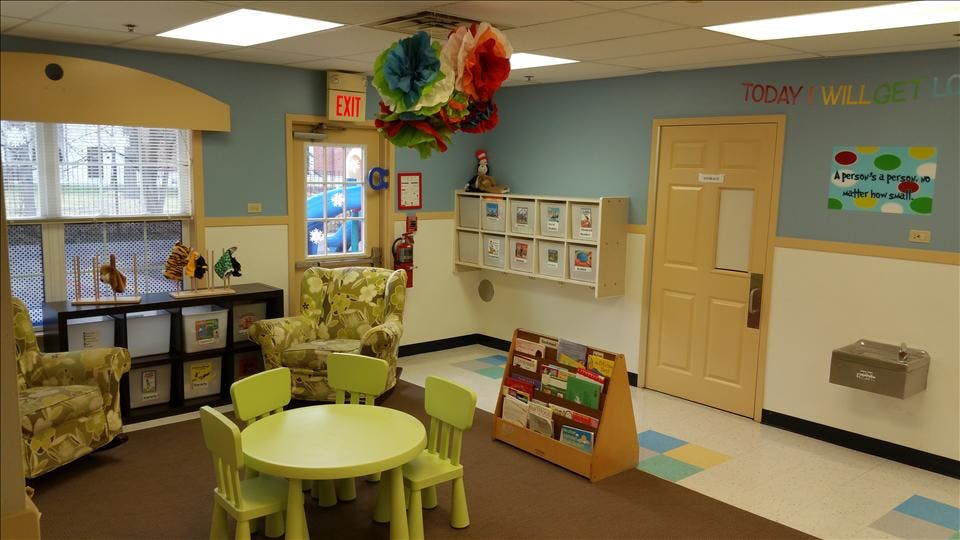 Children's classroom with small green table and chairs, two armchairs, book shelves