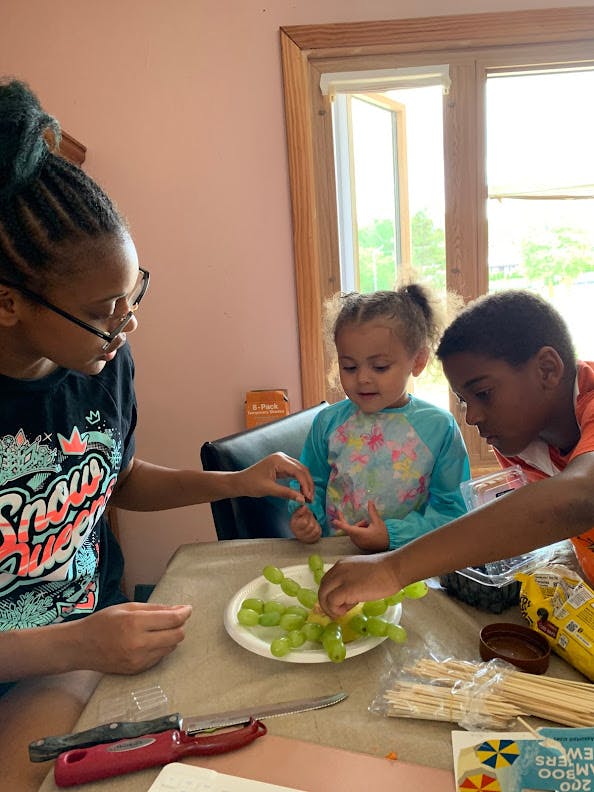Three children making fruit skewers at a table