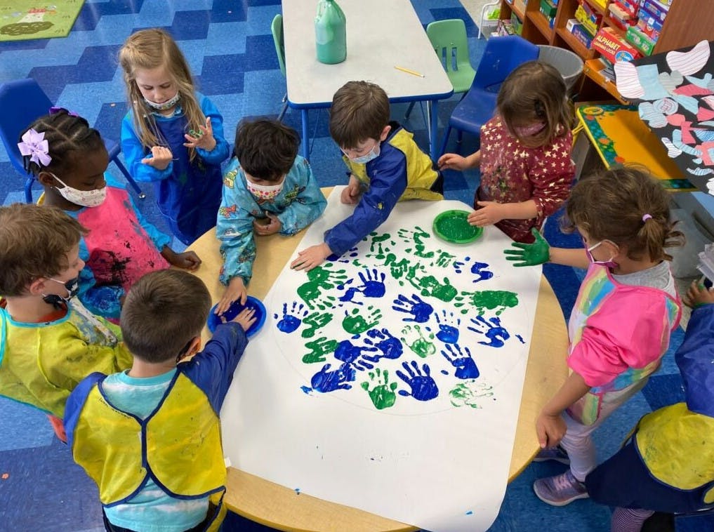 Children making handprints with blue and green paint on a large white paper