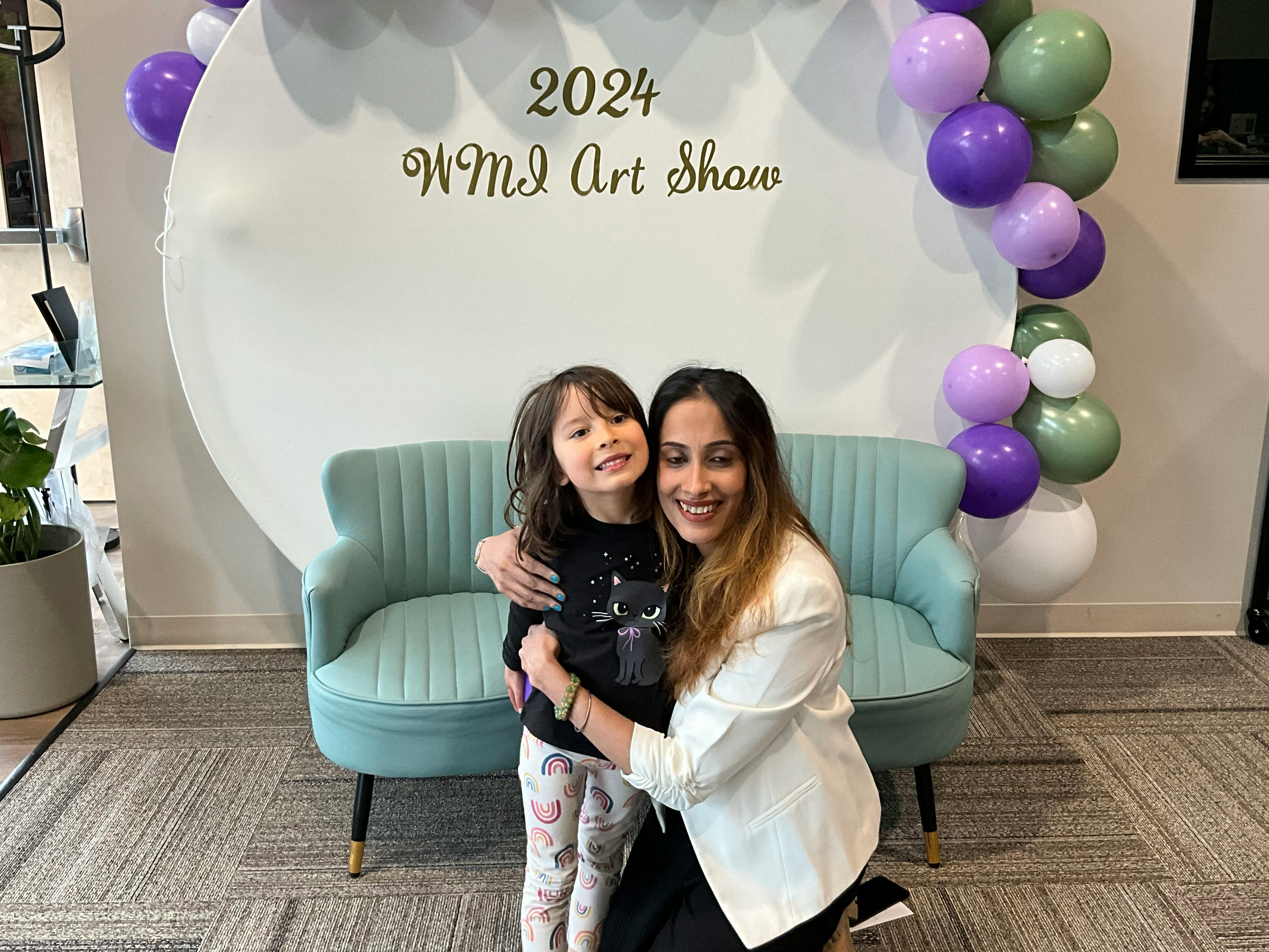Person and child embracing in front of a sign that reads "2024 WMI Art Show"