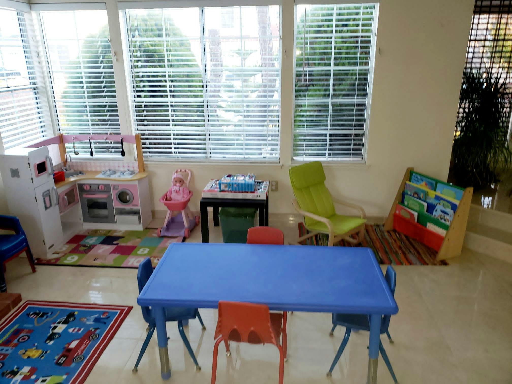Playroom with a blue table, chairs, toy kitchen, and book display