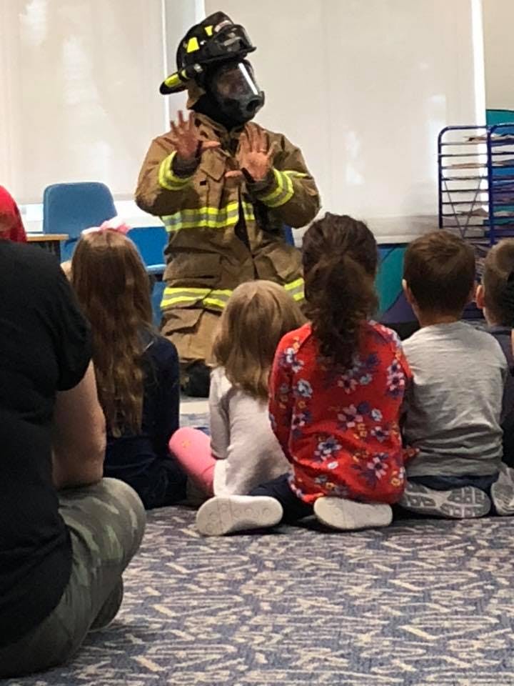 Person in firefighter gear speaking to children sitting on the floor