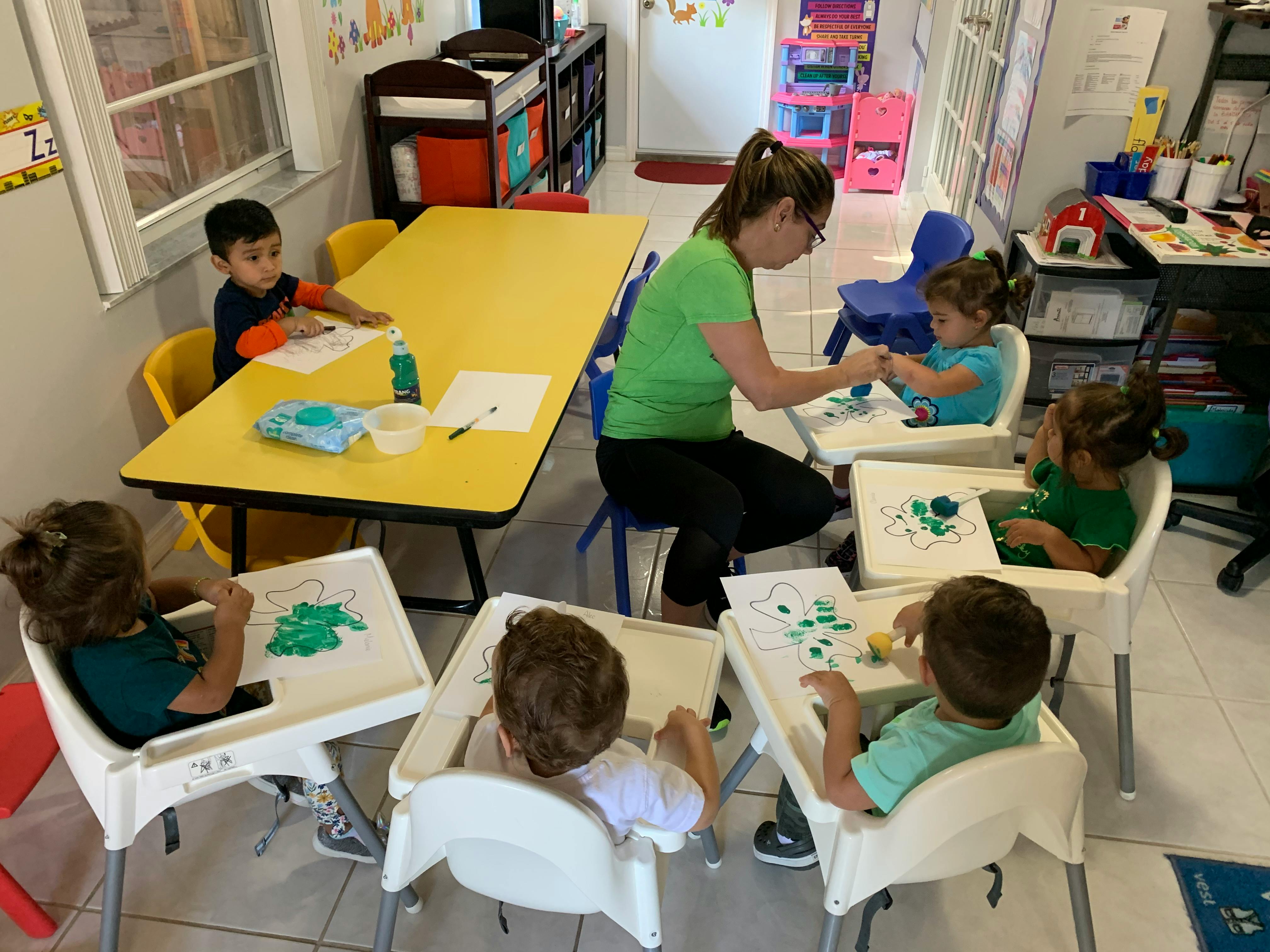 Adult and children painting at tables in a classroom