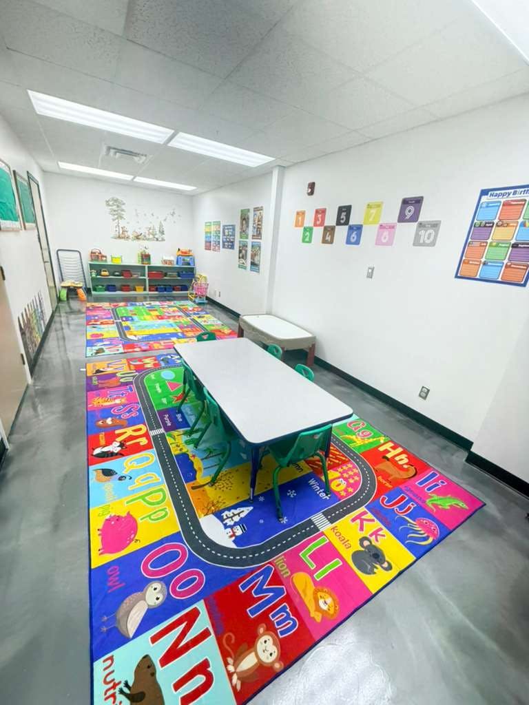 empty classroom with colorful alphabet rug, child-sized tables and chairs