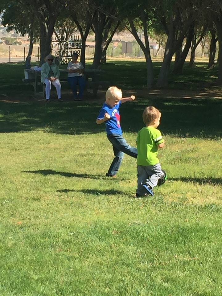 Two children playing on grass, one kicking
