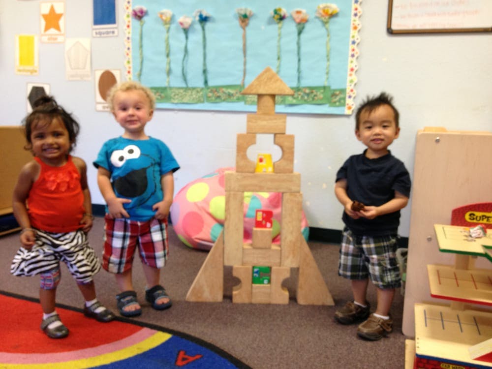 Three children standing next to a large wooden block structure