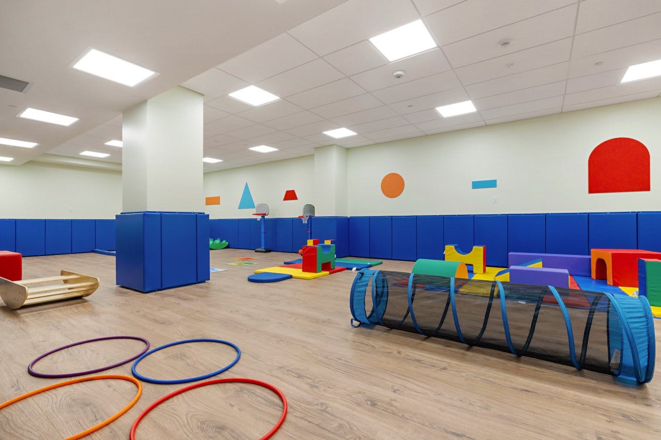 Colorful playroom with soft play equipment, hoops, a tunnel, and padded walls