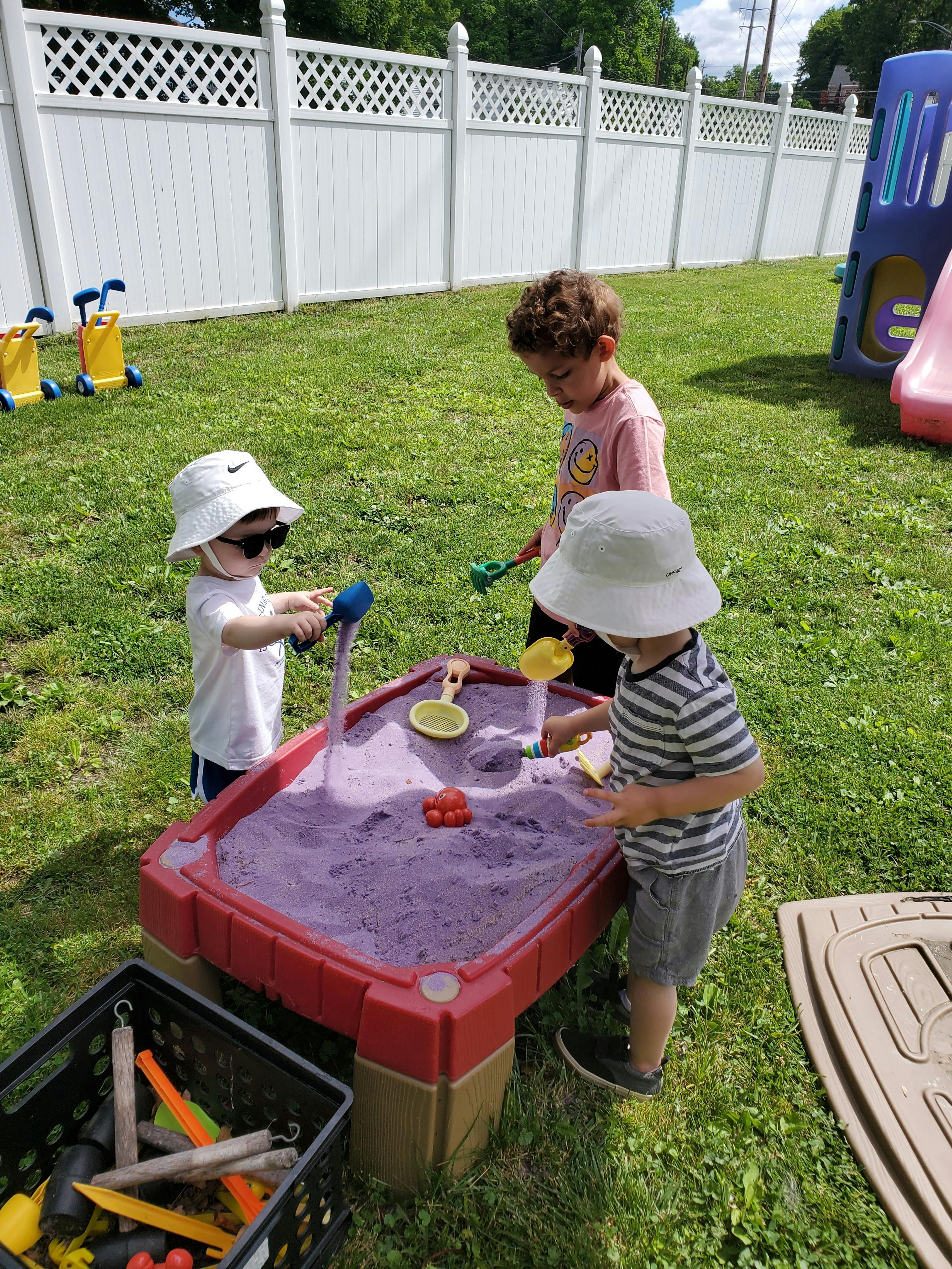 Three children playing with sand in a sand table outdoors