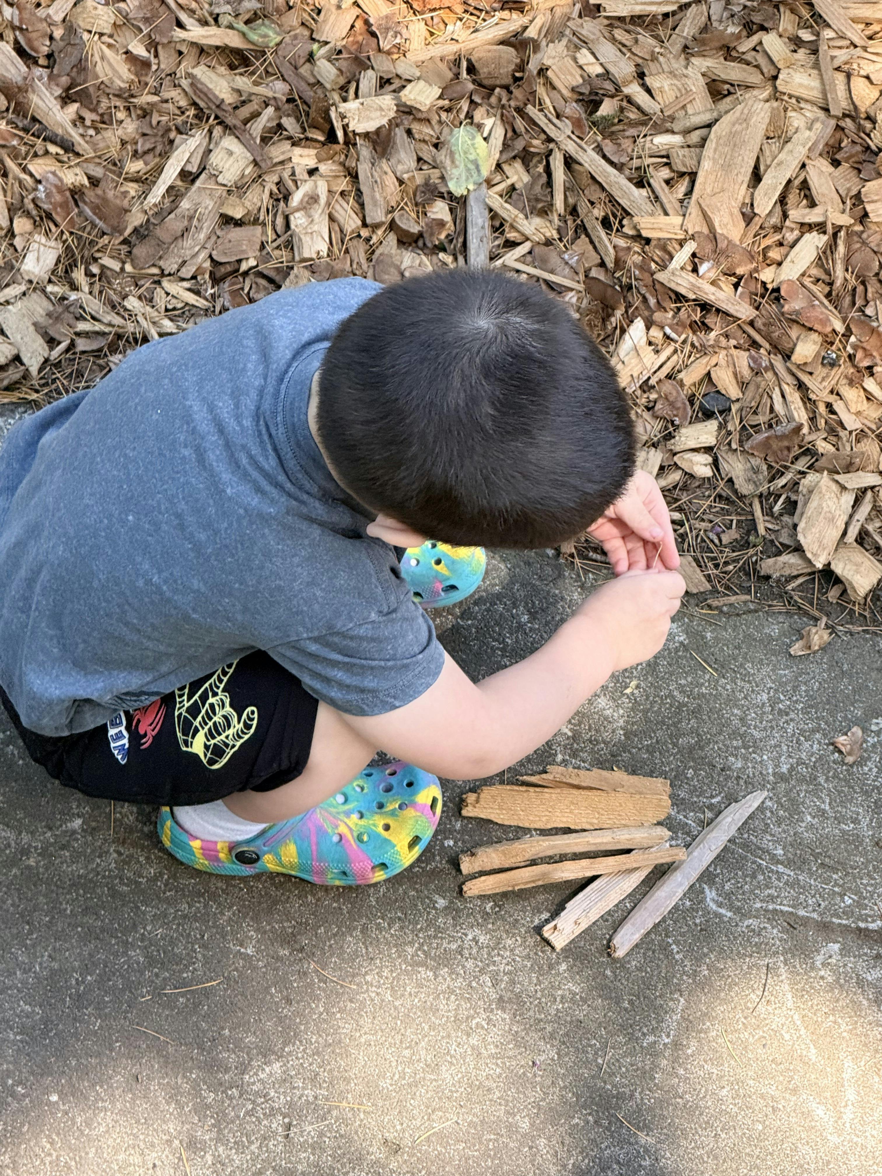 Child crouching on pavement and playing with pieces of wood