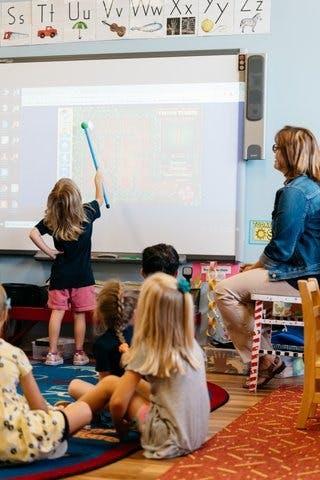 Child pointing at a whiteboard with a stick in a classroom