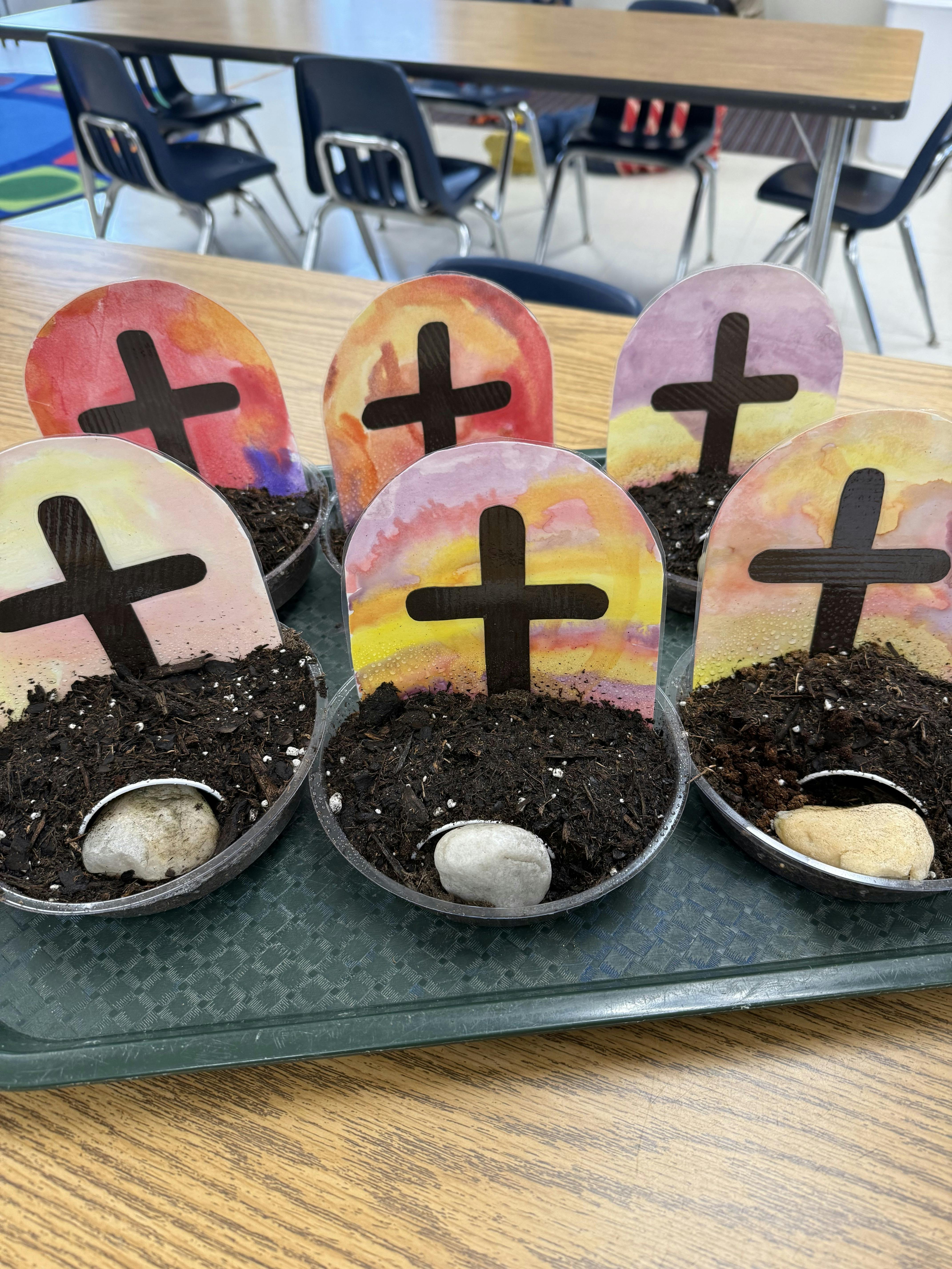 Classroom art project with five cups of dirt with crosses and white rocks