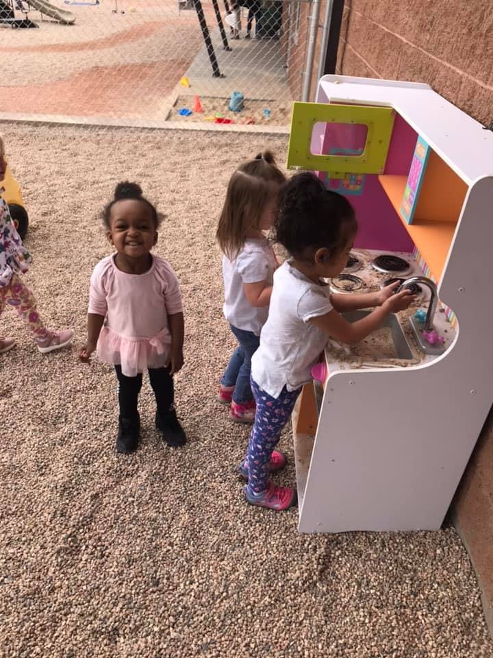 Three children playing with a toy kitchen set outdoors