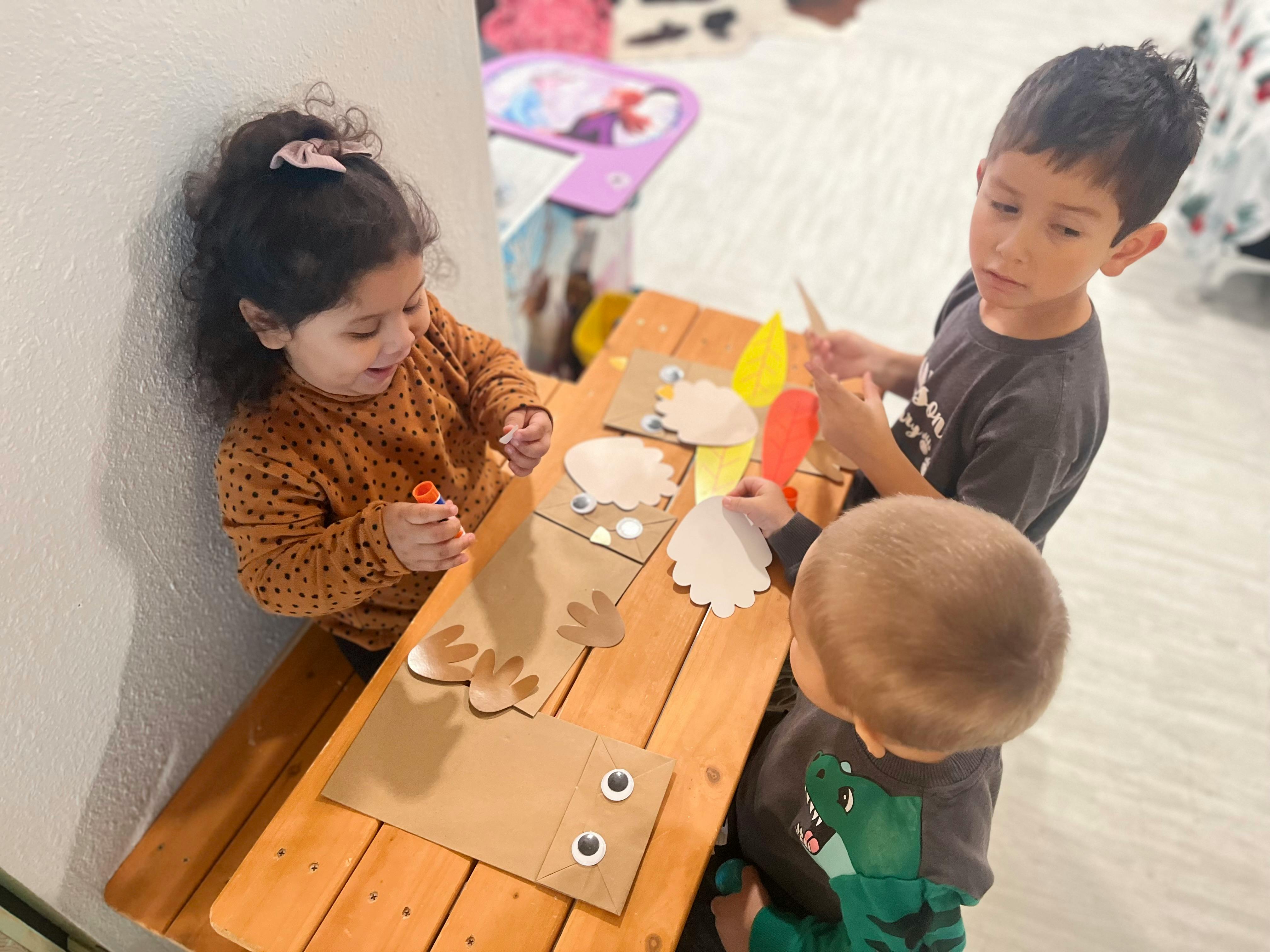 Three children doing crafts at a wooden table