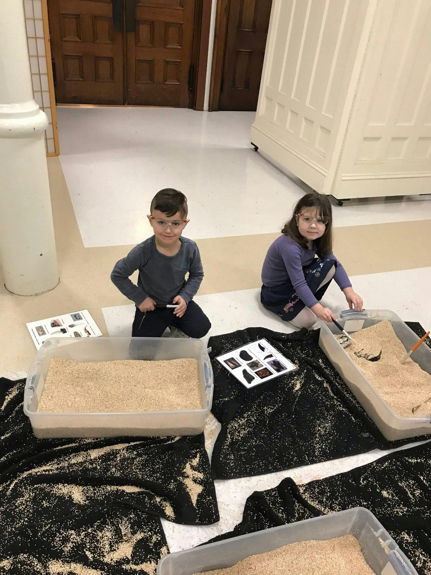 Two children kneeling on the floor with sand trays