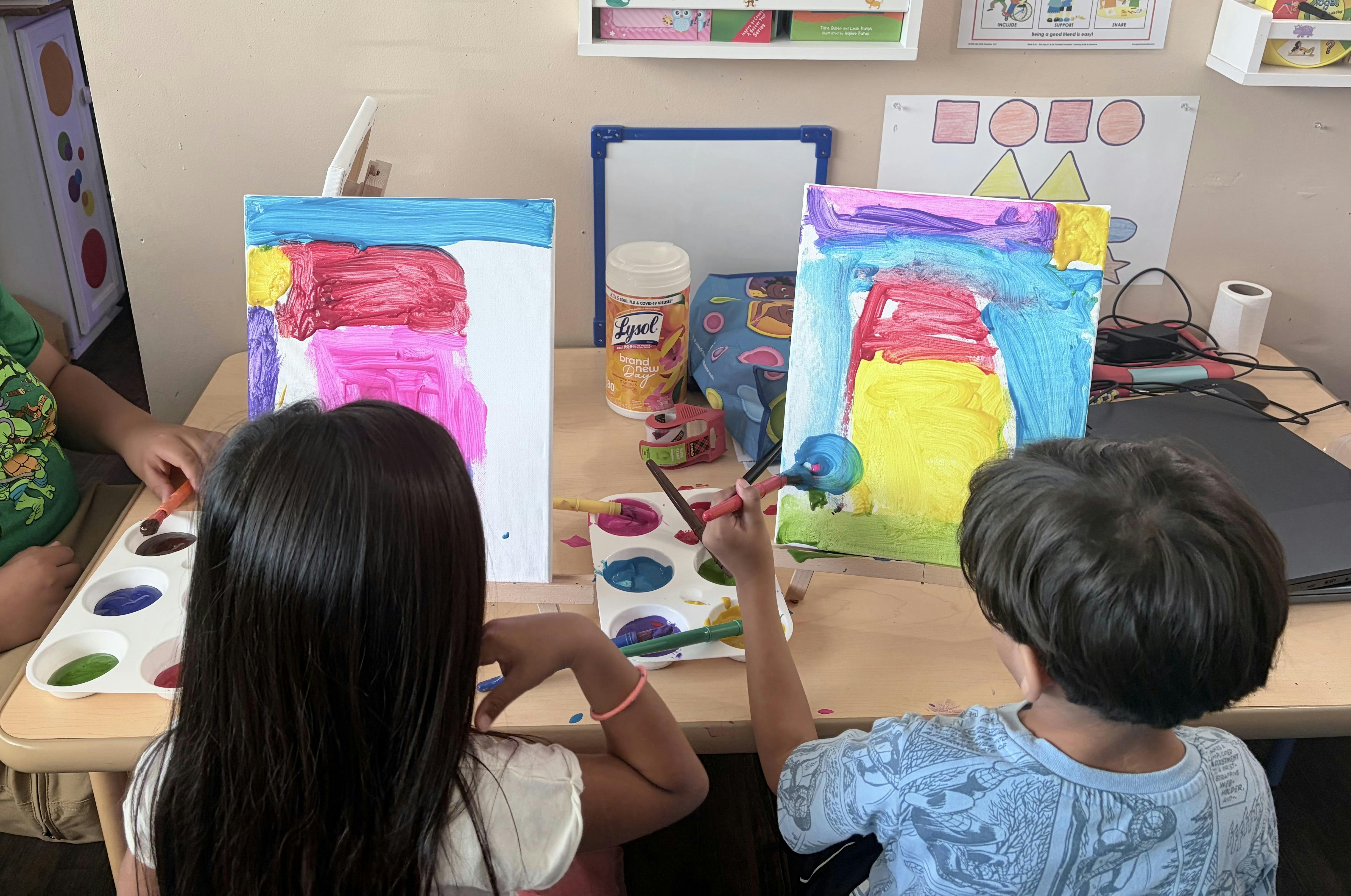 Children painting on canvases at a table in a classroom