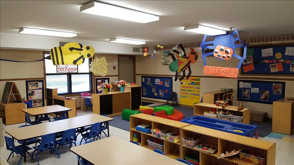 A colorful classroom with tables, chairs, shelving with toys, and bug-themed decorations