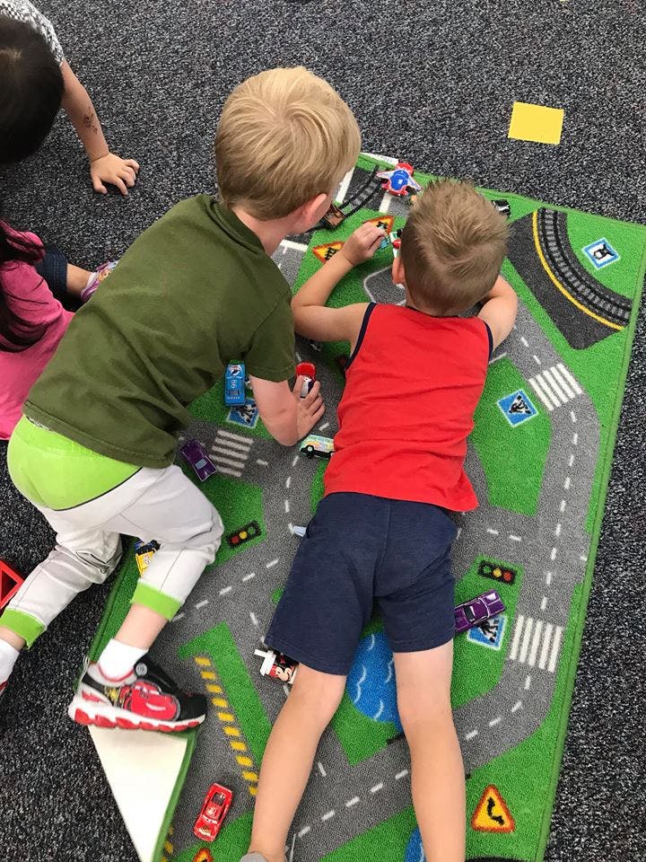 Two children playing with toy cars on a road map rug