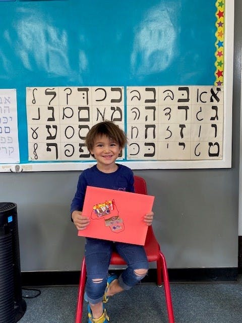 Child sitting on a red chair holding up a red paper craft