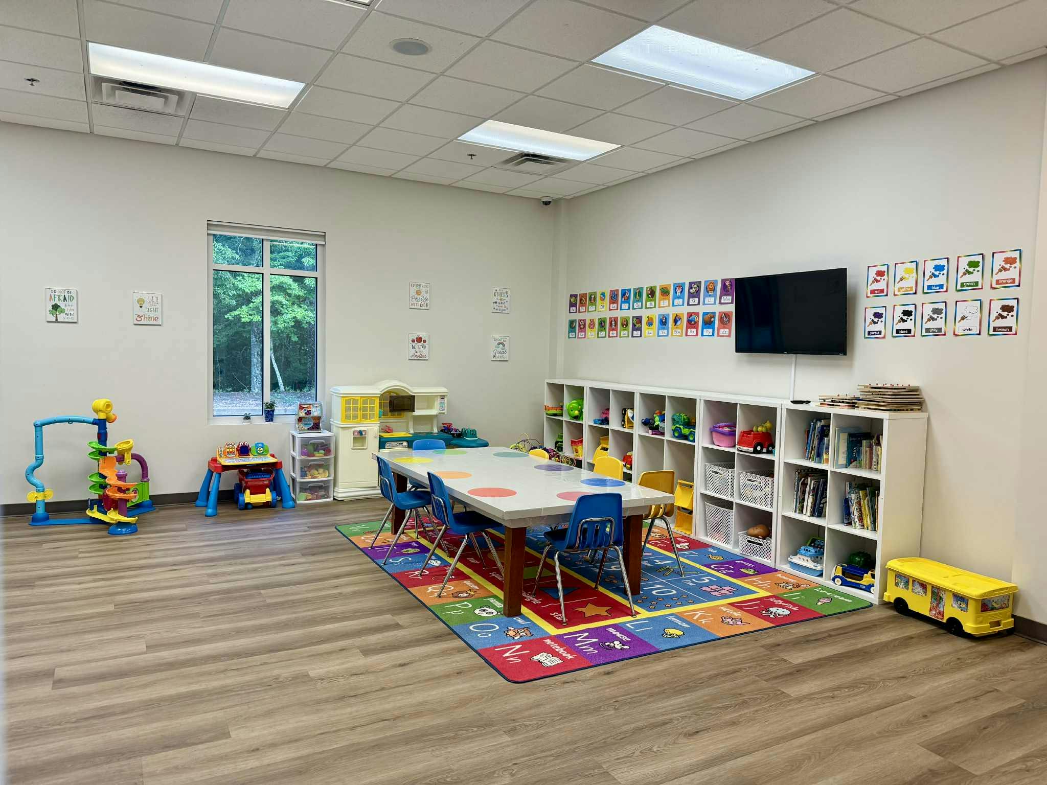 A brightly lit classroom with a large table and chairs on a colorful rug