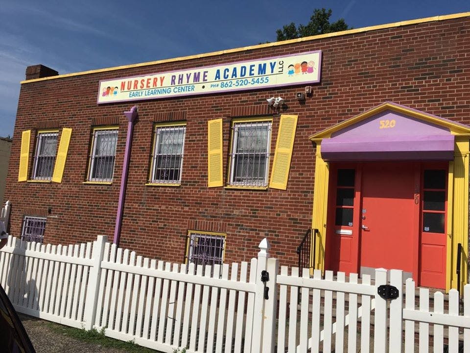 Brick building with sign "Nursery Rhyme Academy" and white picket fence