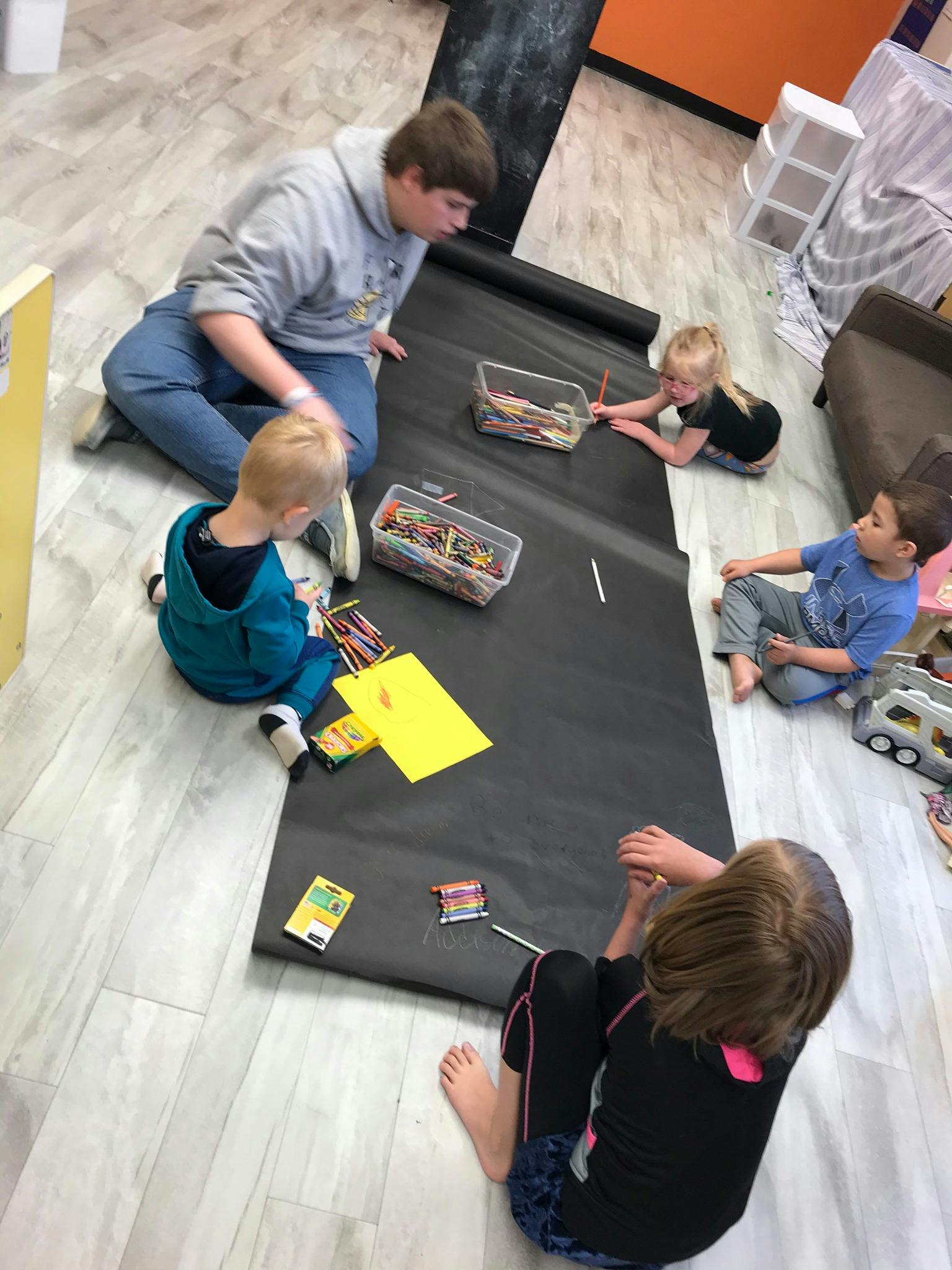 Person and children drawing on a large sheet of paper on the floor