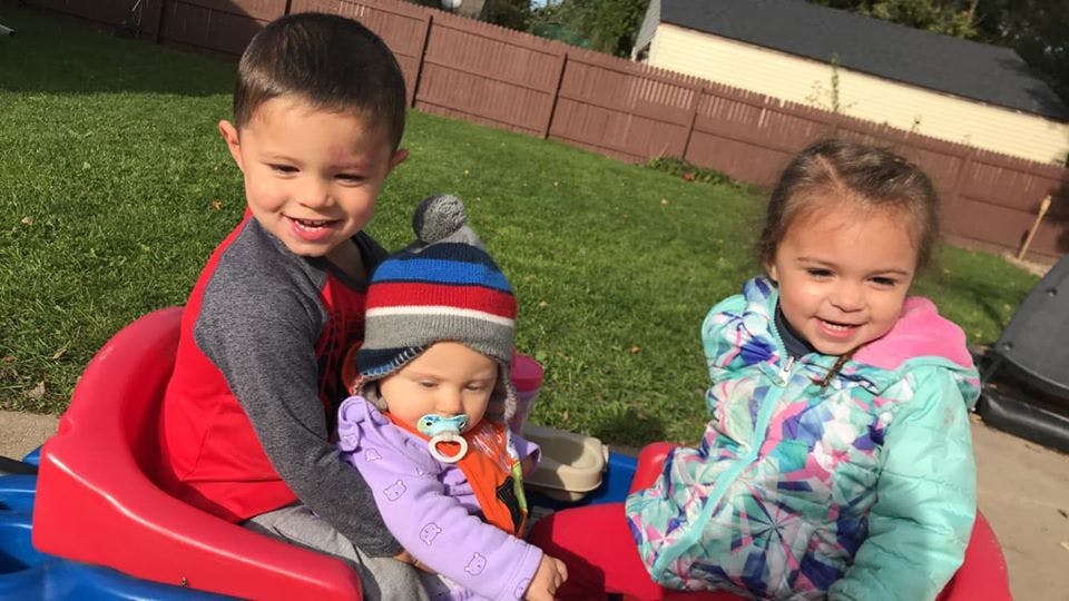 Three children sitting in a red and blue toy car
