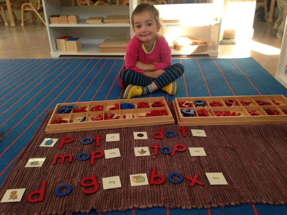 Child sitting on floor with letter tiles and wooden boxes