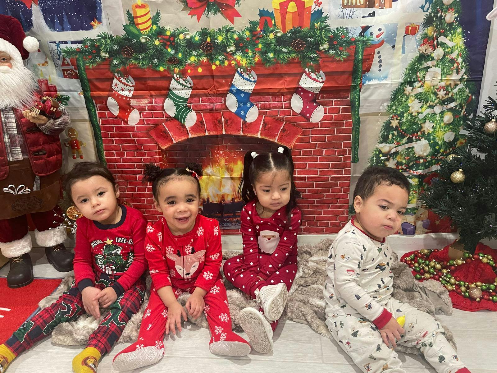 Four children sitting in Christmas pajamas in front of a Christmas backdrop