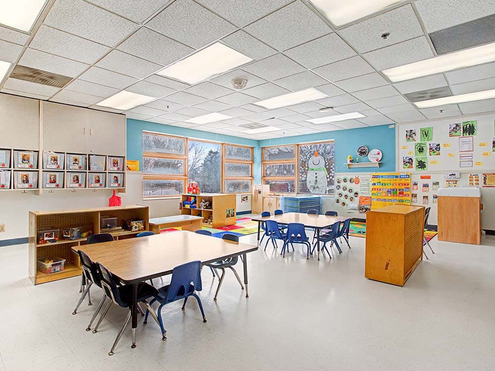 Empty classroom with small tables and chairs, large windows, and colorful decorations