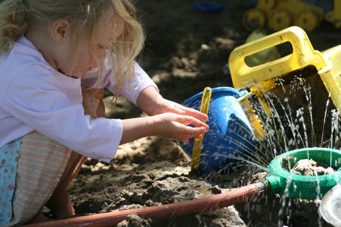 Child playing in sand with water, hands cupped